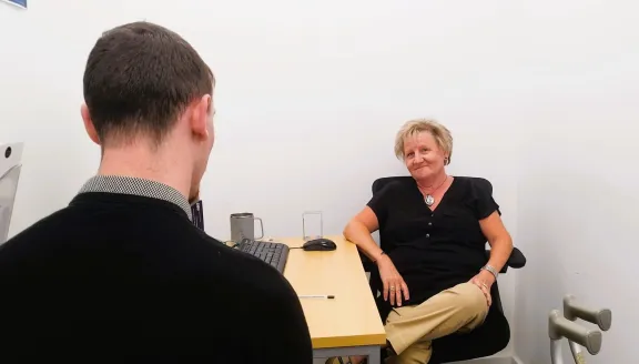 Carol, our generalist volunteer adviser, sitting by her desk in the office helping a client.